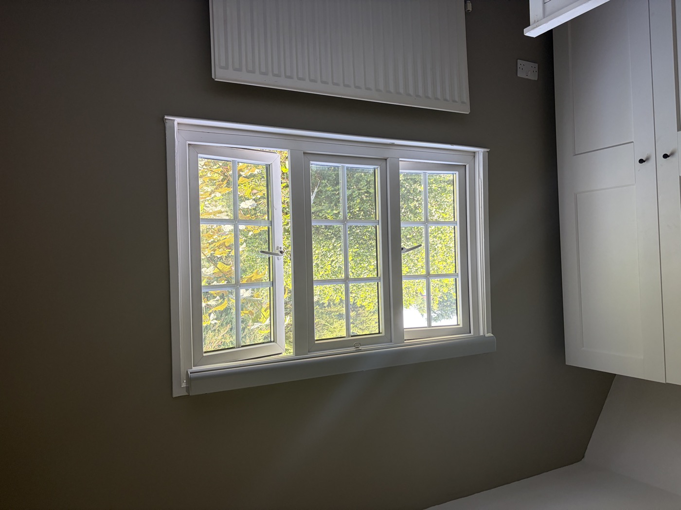 Bedroom after plastering and decorating — dark taupe walls, sash window, fitted wardrobe